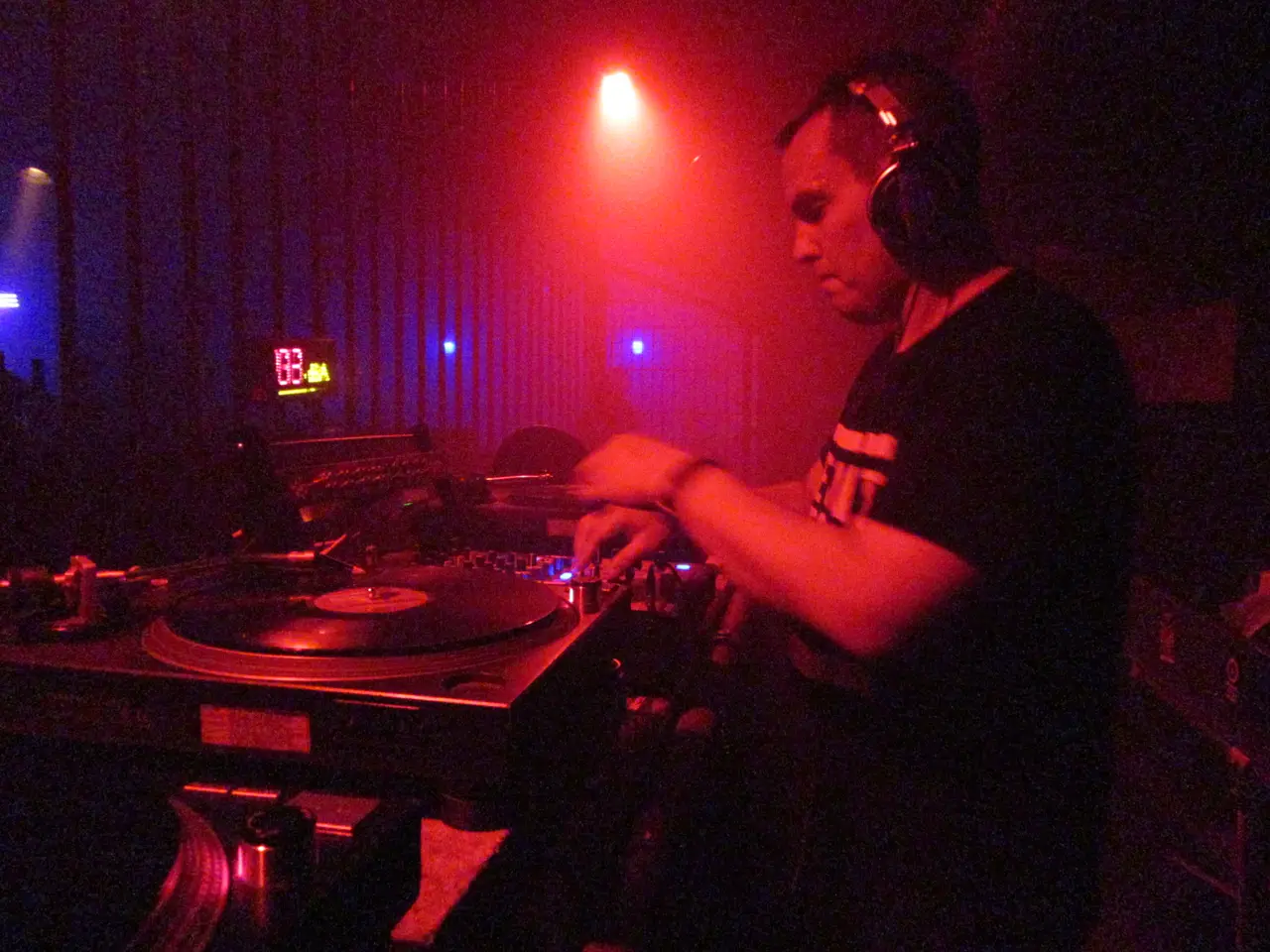 DJ de camiseta negra y audífonos mezclando en un plato de vinilo bajo un haz de luz roja.