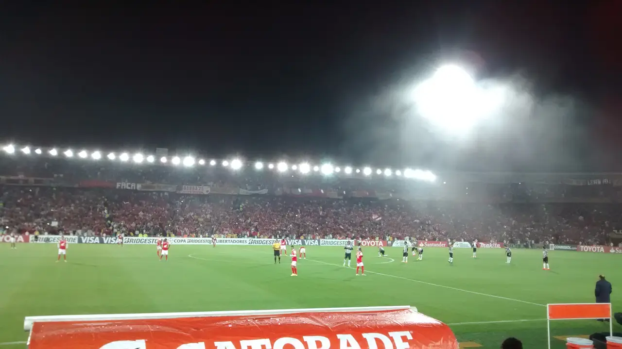 Panorámica nocturna de un estadio con hileras de reflectores y las tribunas llenas durante un partido.