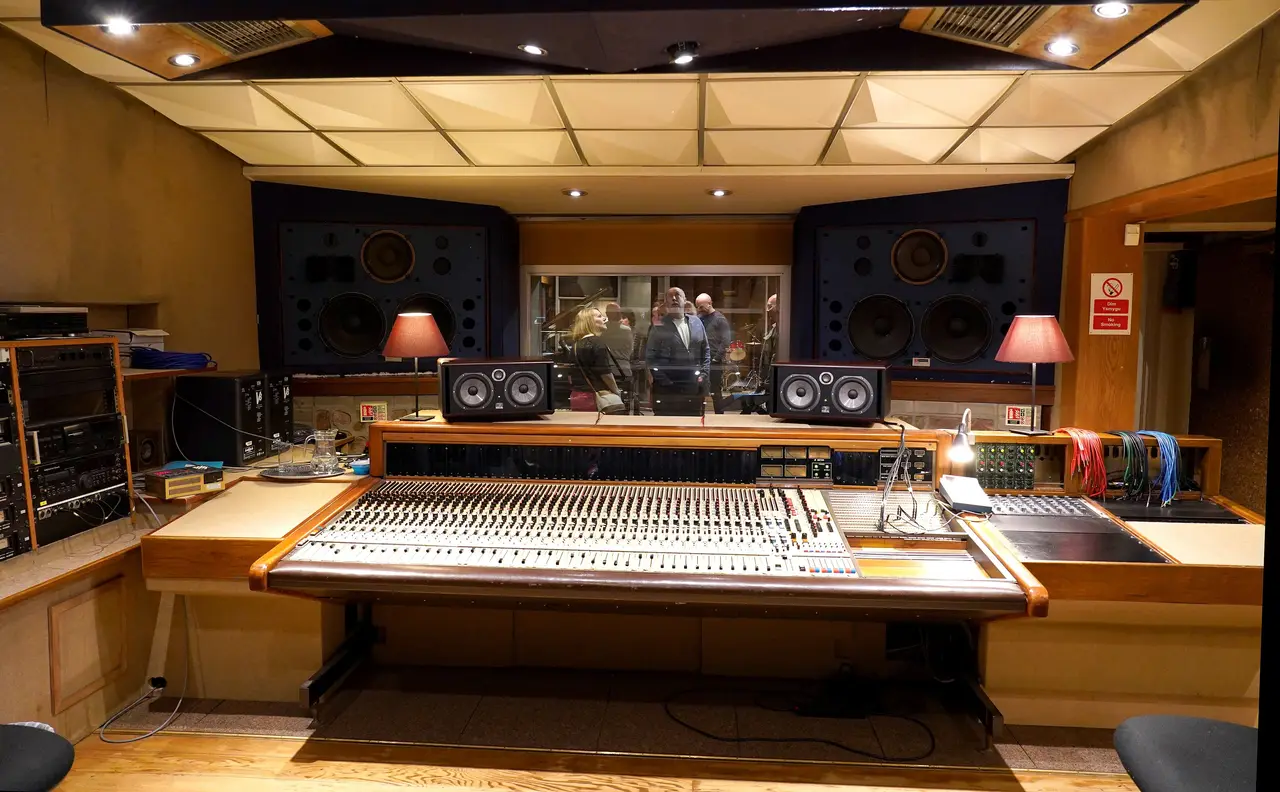Sala de control de estudio con monitores, consola y paneles de madera con luz cálida.